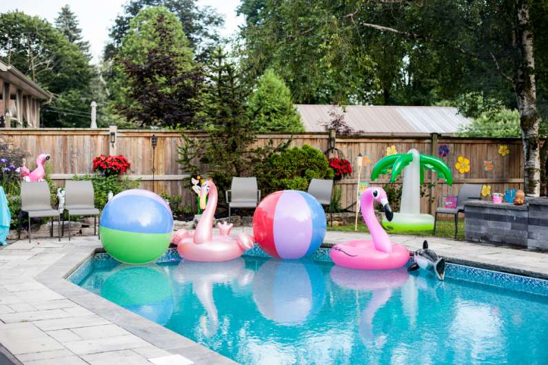 A family pool in the backyard with fun pool floats in one end and festive yard ornaments scattered around the grass.