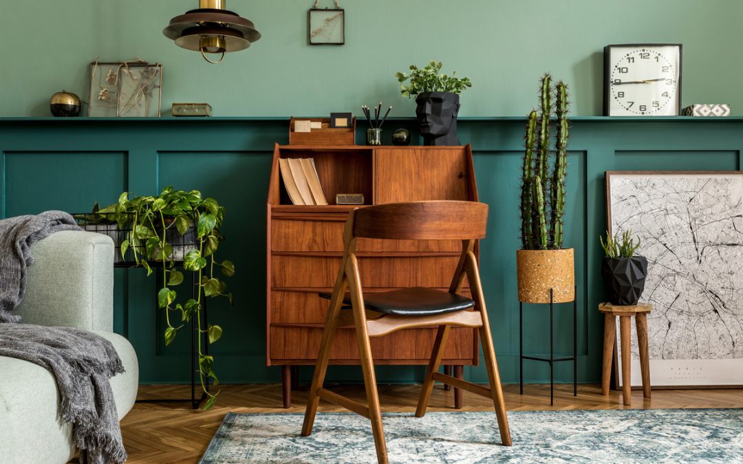 A wooden desk and chair against an emerald green wall. There are plants near the desk and artwork on the right.